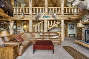 Oversized living room featuring rustic walls and railing, high vaulted ceiling, a wooden ceiling with exposed beams, and a stone fireplace