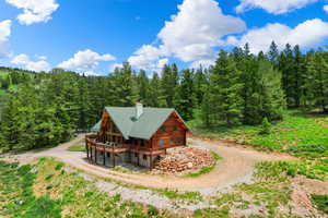 Rear view of property featuring large parking area and trees surrounding this log home