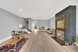 Living room with stairway, wood finished floors, recessed lighting, a tiled fireplace, and an accent wall