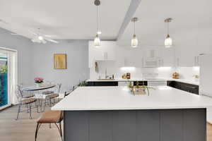 Kitchen with white appliances, white cabinetry, light wood-style flooring, modern cabinets, and decorative light fixtures