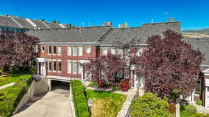 Townhome / multi-family property with roof with shingles, brick siding, driveway, and an attached garage