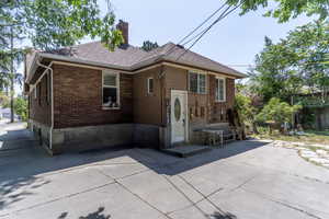 Rear view of property featuring a chimney, brick siding, a patio, and a shingled roof