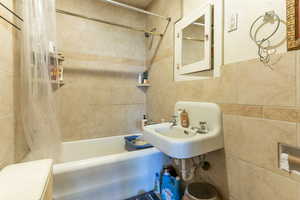 Bathroom featuring shower / bathtub combination with curtain, tile walls, and pet washing station