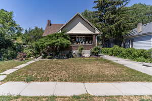 View of front of property with a front yard, a chimney, a porch, and brick siding