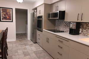 Kitchen featuring appliances with stainless steel finishes, tasteful backsplash, stone finish flooring, and light countertops