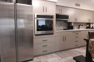 Kitchen with stainless steel appliances, tasteful backsplash, stone finish flooring, and light countertops