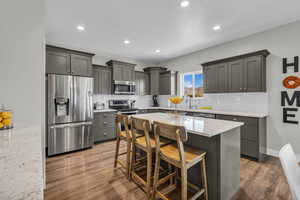Kitchen featuring appliances with stainless steel finishes, quartz countertops, a breakfast bar area, tasteful backsplash, and light wood-style flooring