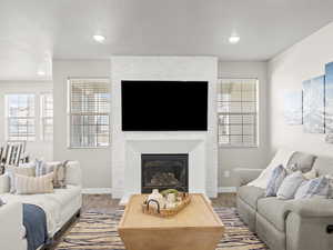 Living room with wood finished floors, a large fireplace, and recessed lighting