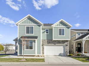 View of front facade featuring board and batten siding, stone siding, driveway, and a garage