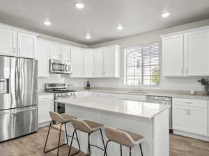 Kitchen featuring stainless steel appliances, a breakfast bar area, white cabinetry, light wood-style flooring, and recessed lighting