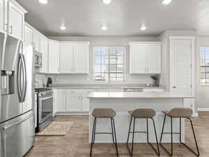Kitchen with stainless steel appliances, a kitchen bar, white cabinets, a kitchen island, and recessed lighting