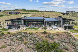 Back of house featuring a chimney, a standing seam roof, stone siding, a metal roof, and a patio area