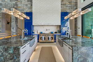 Kitchen with range with two ovens, modern cabinets, a center island with sink, and dark stone counters