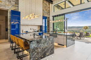 Kitchen with modern cabinets, a towering ceiling, a mountain view, dark stone counters, and a kitchen island with sink