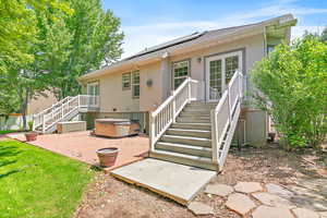 Back of property featuring a hot tub, stairway, a patio, stucco siding, and roof mounted solar panels