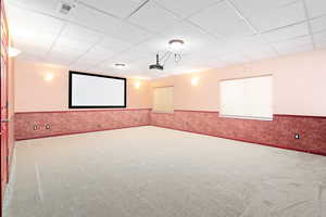 Cinema room with carpet floors, a drop ceiling, a wainscoted wall, and wallpapered walls
