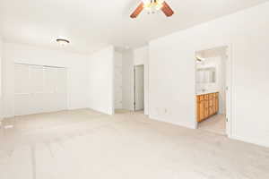 Unfurnished bedroom with light carpet, a closet, ensuite bath, and ceiling fan