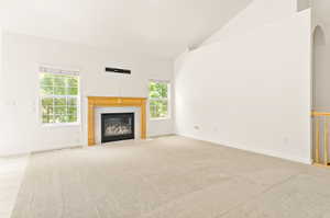 Unfurnished living room featuring healthy amount of natural light, a fireplace with flush hearth, light colored carpet, and high vaulted ceiling