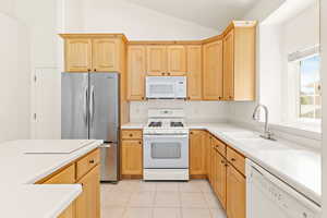 Kitchen featuring white appliances, light brown cabinets, lofted ceiling, light tile patterned floors, and light countertops