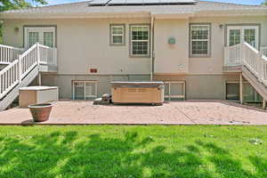 Back of property with a hot tub, a patio, and a yard