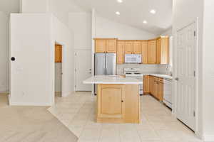 Kitchen with white appliances, a kitchen island, recessed lighting, light countertops, and light brown cabinetry