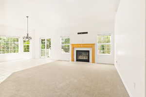 Unfurnished living room featuring a fireplace with flush hearth, a chandelier, light tile patterned floors, and light colored carpet