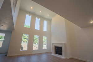 Unfurnished living room with wood finished floors, a glass covered fireplace, recessed lighting, and a high ceiling