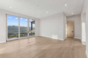 Empty room with a mountain view, light wood finished floors, and recessed lighting