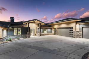 View of front of property with an attached garage, concrete driveway, a chimney, and stone siding