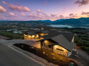 View of front facade with stone siding, a shingled roof, curved driveway, and a water and mountain view
