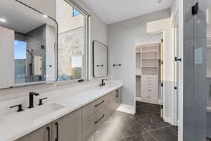 Full bathroom with double vanity, healthy amount of natural light, a spacious closet, and a shower with door