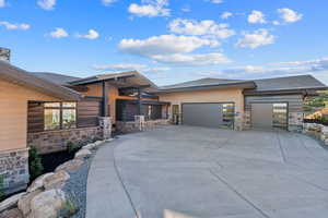 View of front of home featuring stone siding, a garage, a shingled roof, and driveway