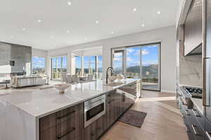 Kitchen with modern cabinets, light wood-type flooring, backsplash, stainless steel appliances, and light stone counters