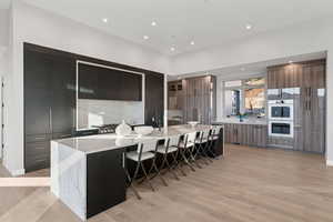 Kitchen with modern cabinets, a spacious island, double wall oven, light stone countertops, and recessed lighting