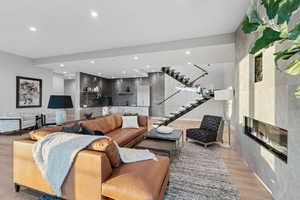 Living area featuring a glass covered fireplace, light wood-type flooring, recessed lighting, and stairway