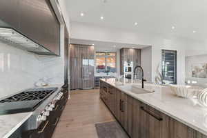 Kitchen featuring modern cabinets, appliances with stainless steel finishes, light wood-style floors, decorative backsplash, and light stone counters