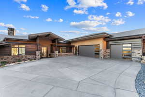 Prairie-style home with stone siding, a garage, driveway, and a chimney