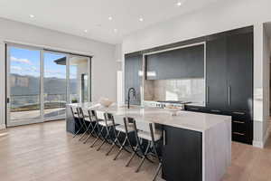 Kitchen featuring dark cabinetry, modern cabinets, a large island, decorative backsplash, and light wood-style floors