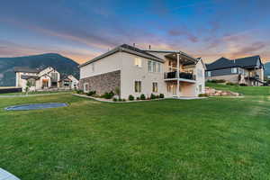 Rear view of house with a balcony, stone siding, a yard, stucco siding, and a patio area