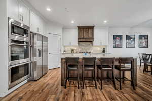 Kitchen with stainless steel appliances, light countertops, wood finished floors, decorative backsplash, and white cabinetry