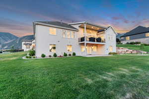 Back of property with a balcony, a lawn, stucco siding, a patio, and a mountain view