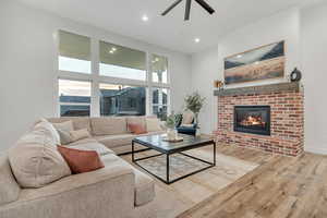 Living room with a brick fireplace, a ceiling fan, wood finished floors, and recessed lighting