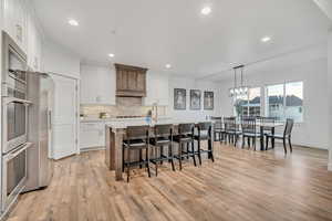 Kitchen with a kitchen bar, light countertops, white cabinets, stainless steel appliances, and tasteful backsplash
