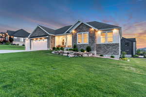 Craftsman inspired home with stone siding, a yard, an attached garage, concrete driveway, and a shingled roof