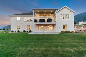 Rear view of property with a patio, stucco siding, a yard, a mountain view, and a balcony