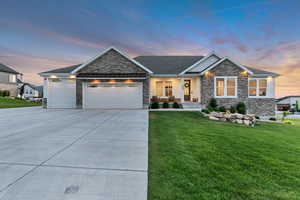 Craftsman-style home featuring stone siding, a front lawn, a garage, concrete driveway, and covered porch