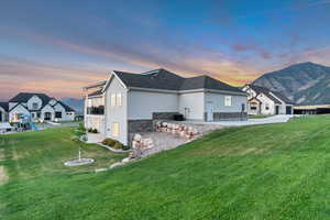 Property exterior at dusk with stucco siding, stone siding, a lawn, and a mountain view
