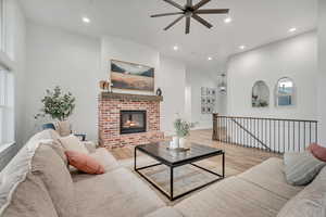 Living room with ceiling fan, wood finished floors, recessed lighting, a brick fireplace, and healthy amount of natural light