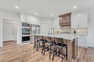 Kitchen featuring appliances with stainless steel finishes, light wood-type flooring, a kitchen breakfast bar, backsplash, and light countertops