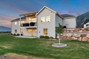 Back of property at dusk with a balcony, a patio, a yard, stucco siding, and a mountain view